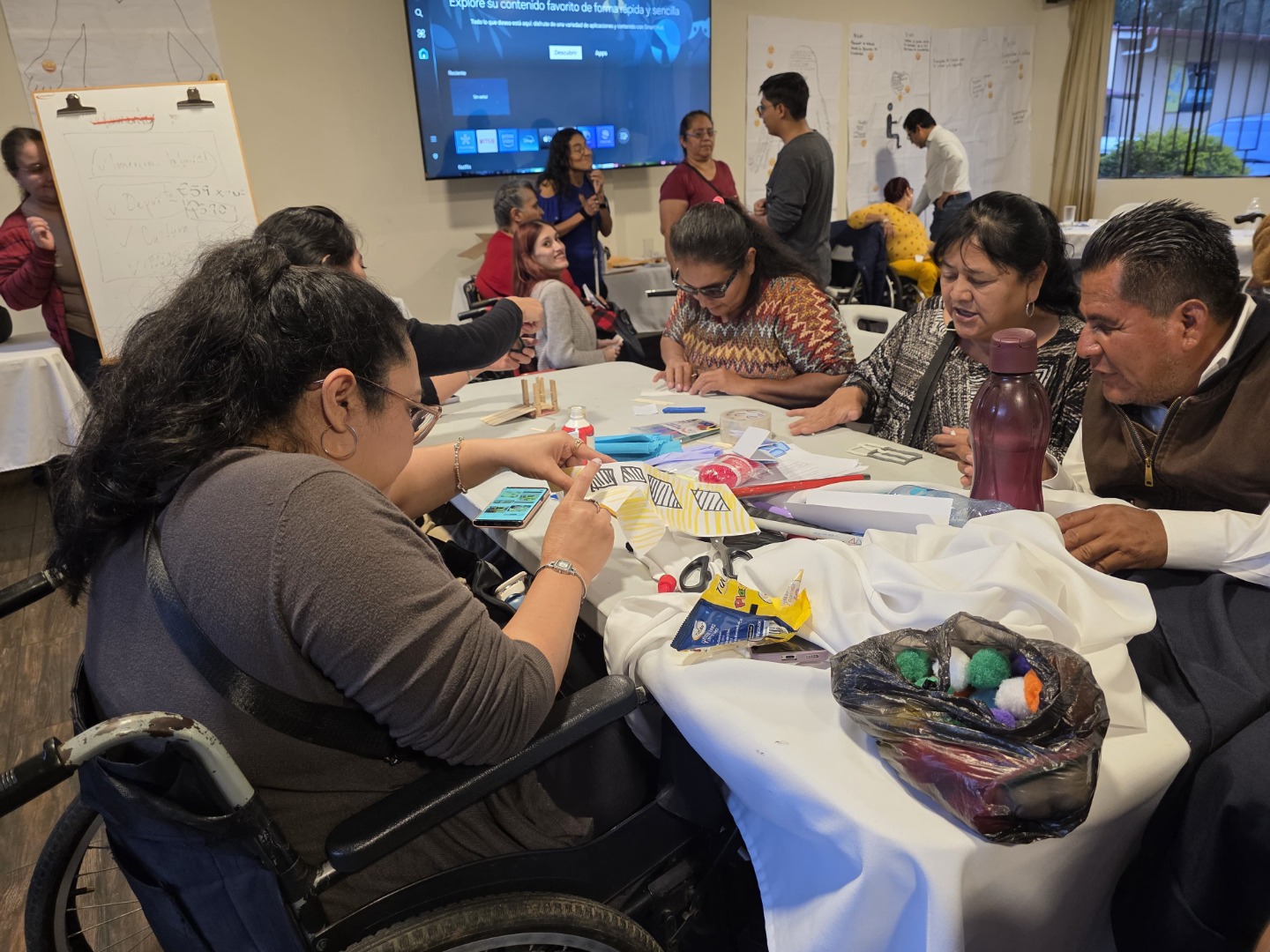 Actividad integradora "Espacios con accesibilidad" Uno de los momentos del taller fue el elaborar una ciudad accesible e inclusiva, promoviendo los derechos de las personas con discapacidad y la participación que deben tener las asociaciones a través de la integración de los sectores. Texto alternativo: Personas alrededor de una mesa trabajan con papel, marcadores y materiales de manualidades. Una persona en silla de ruedas dibuja.